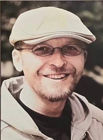 Uśmiechnięty Marcin Wierzba w jasnym kaszkiecie i okularach.